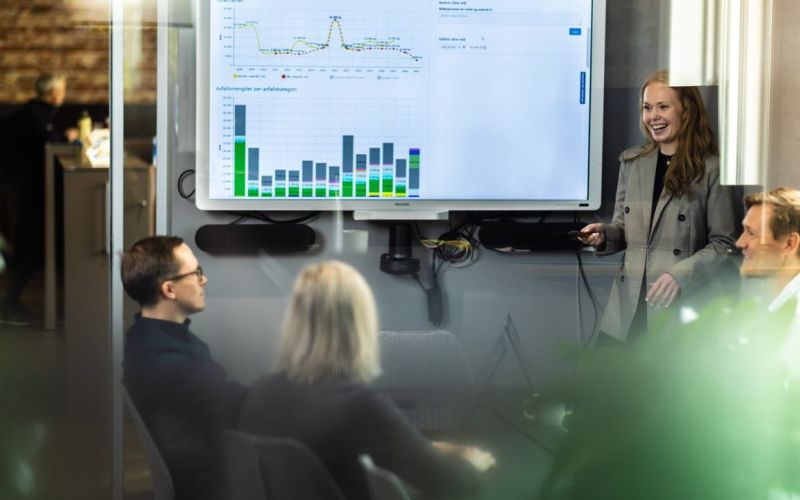 Bilde av en gruppe mennesker i møterom som ser på stor statistikkdata på skjerm