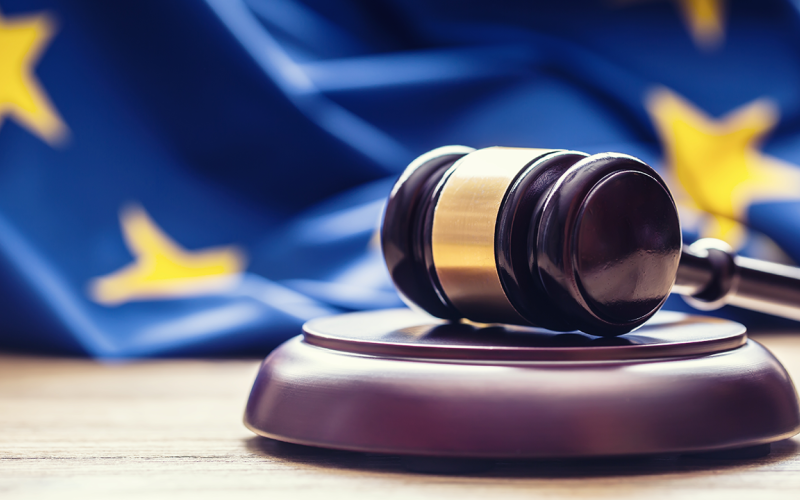 Bilde av en lov-hammer på et bord, og med et EU-flagg i bakgrunnen