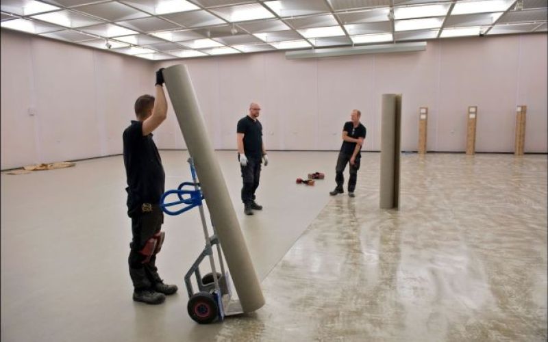 Tre menn som jobber med gulvbelegg i lokale