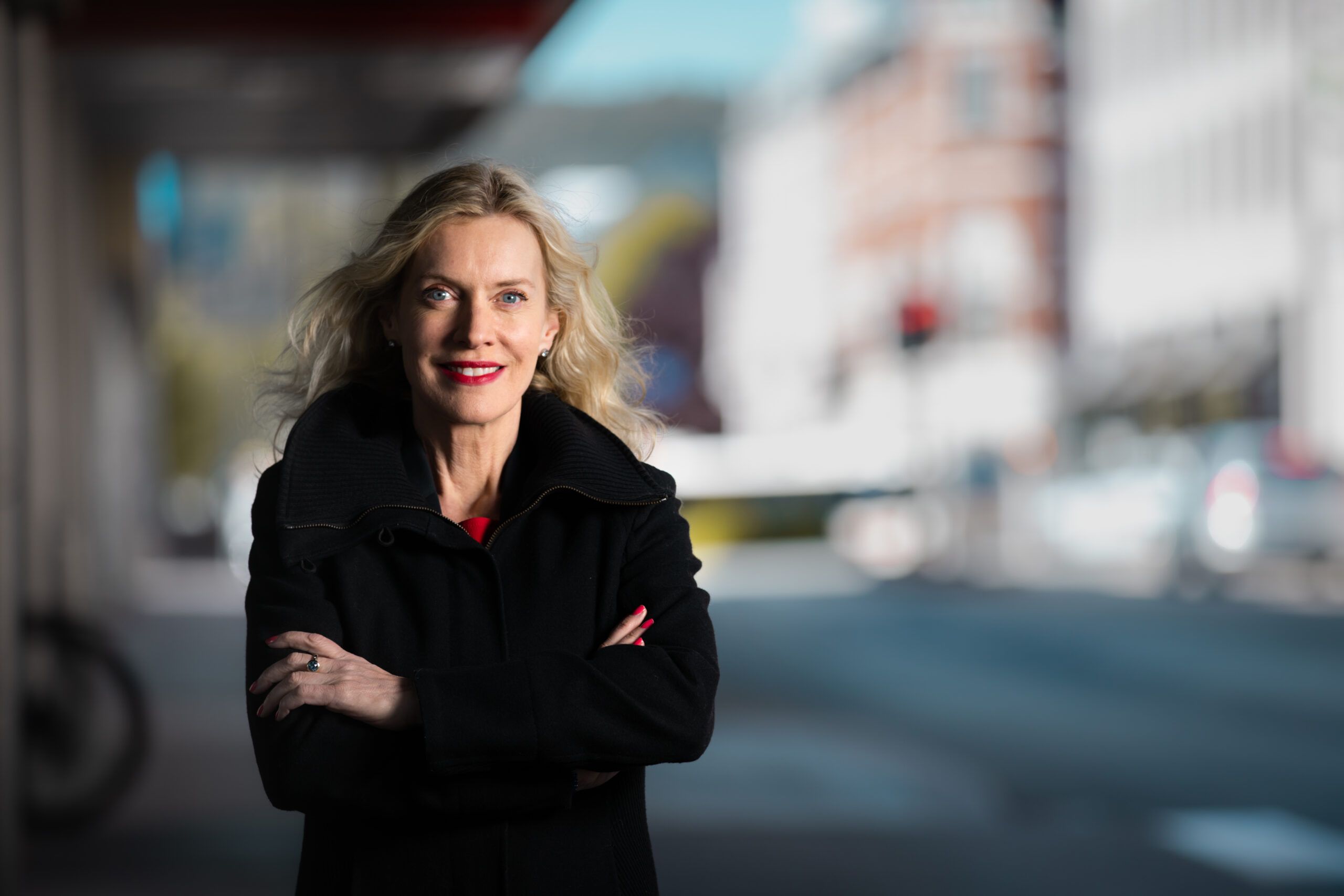 Dame med armene i kors poserer med bybakgrunn