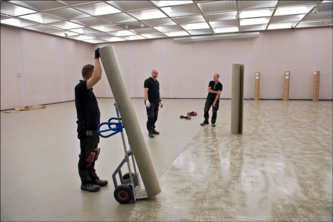 Tre menn som jobber med gulvbelegg i lokale